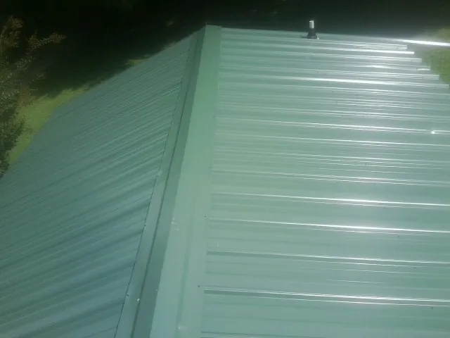 New green metal panels meeting at the ridge of a roof — Flat Roof Repair work by our crew in Fort Montgomery