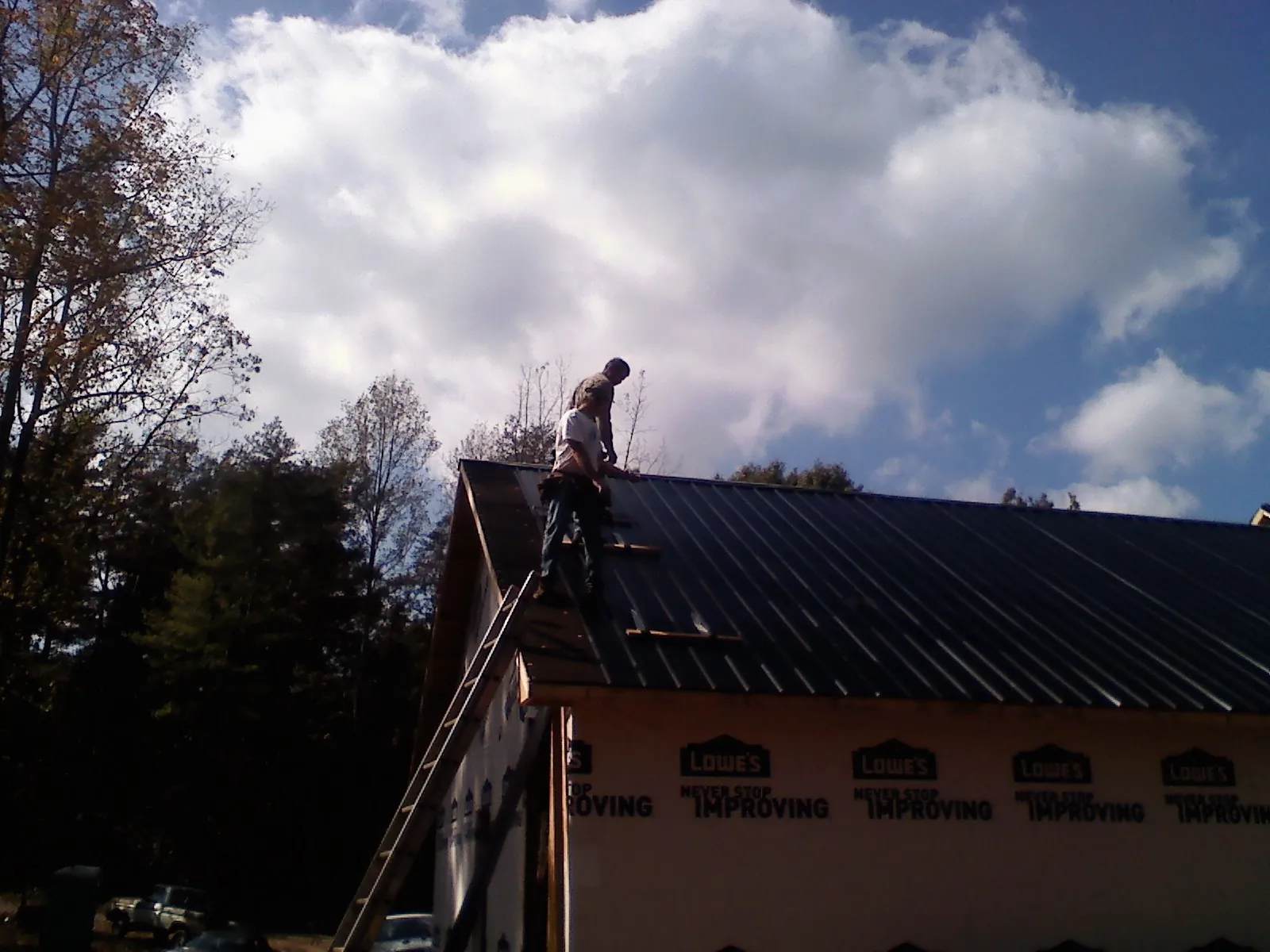 Roofer fastening dark metal panels high against a cloudy sky, from a Roof Inspection job in Fort Montgomery