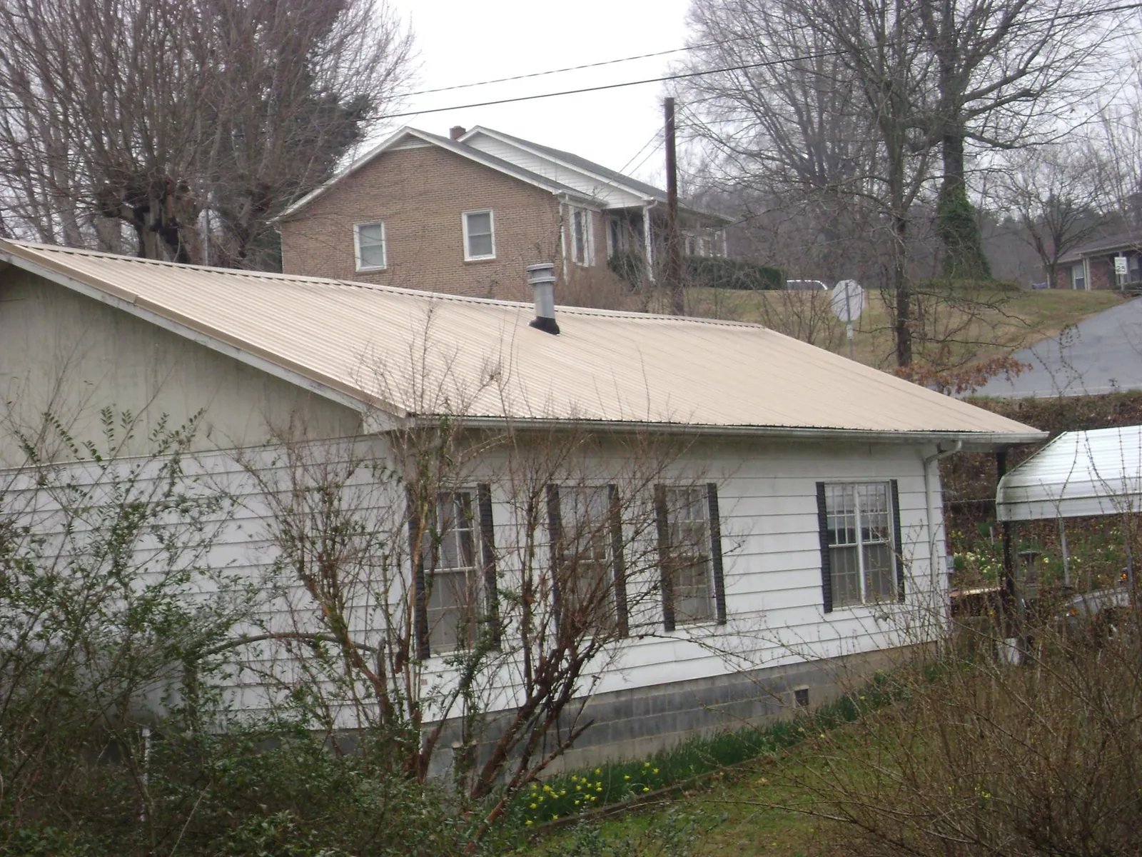 Tan metal roof on a white sided house set into a hillside — Commercial Roofing by Roofing Brothers in Fort Montgomery