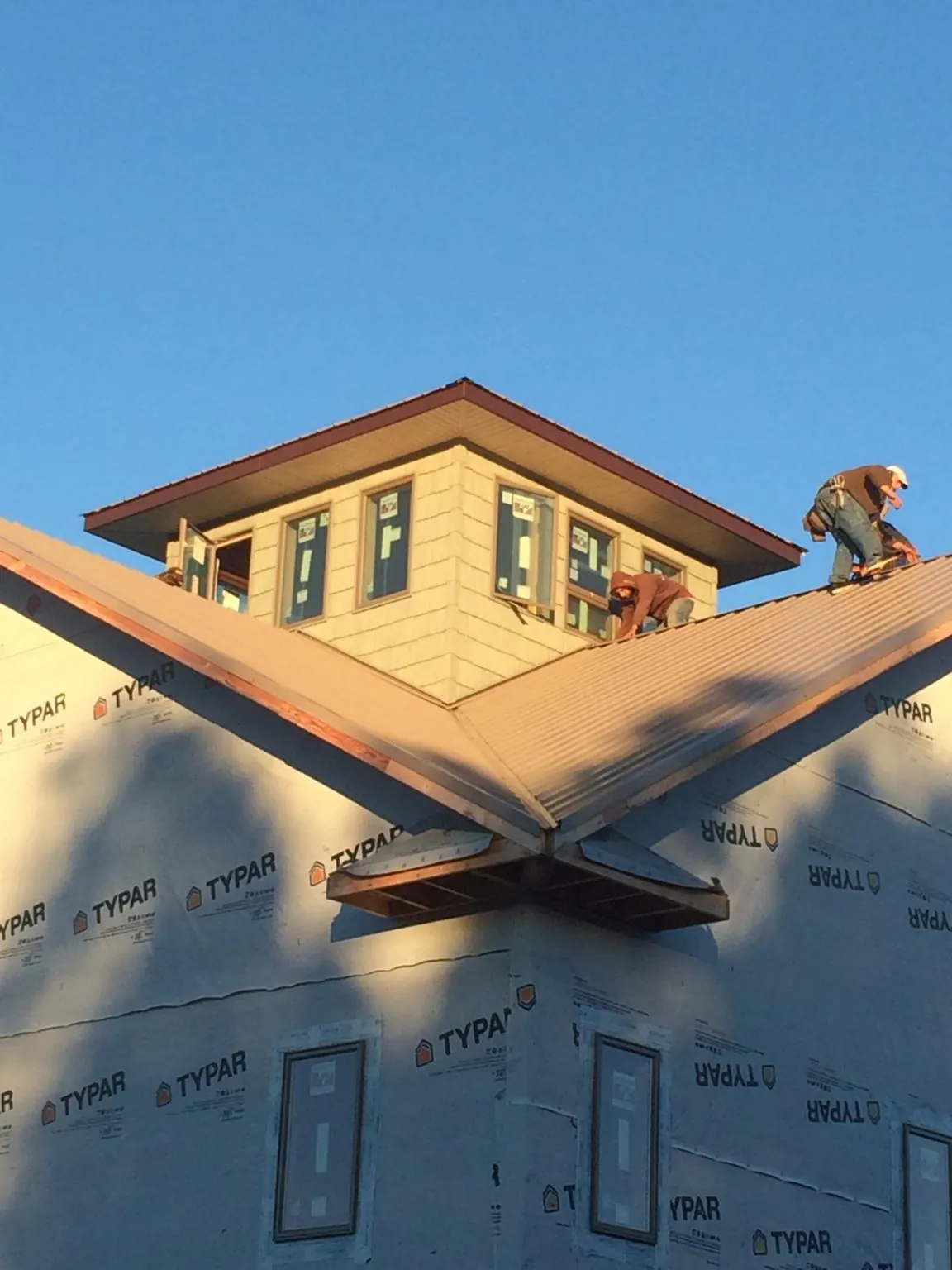 Roofers working around a rooftop cupola on a new metal roof at sunset — Roof Waterproofing in Fort Montgomery by Roofing Brothers